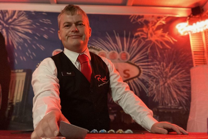 Croupier dealing blackjack, wearing uniform of red tie, waistcoat and name tag