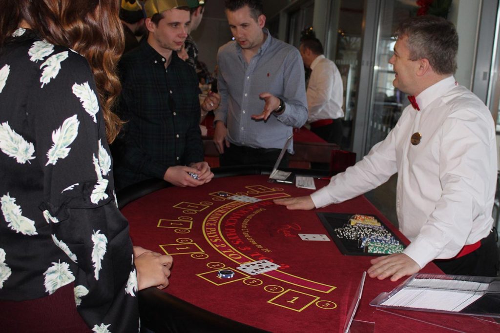 Croupier wearing bowtie and name tag dealing blackjack at fun casino party night
