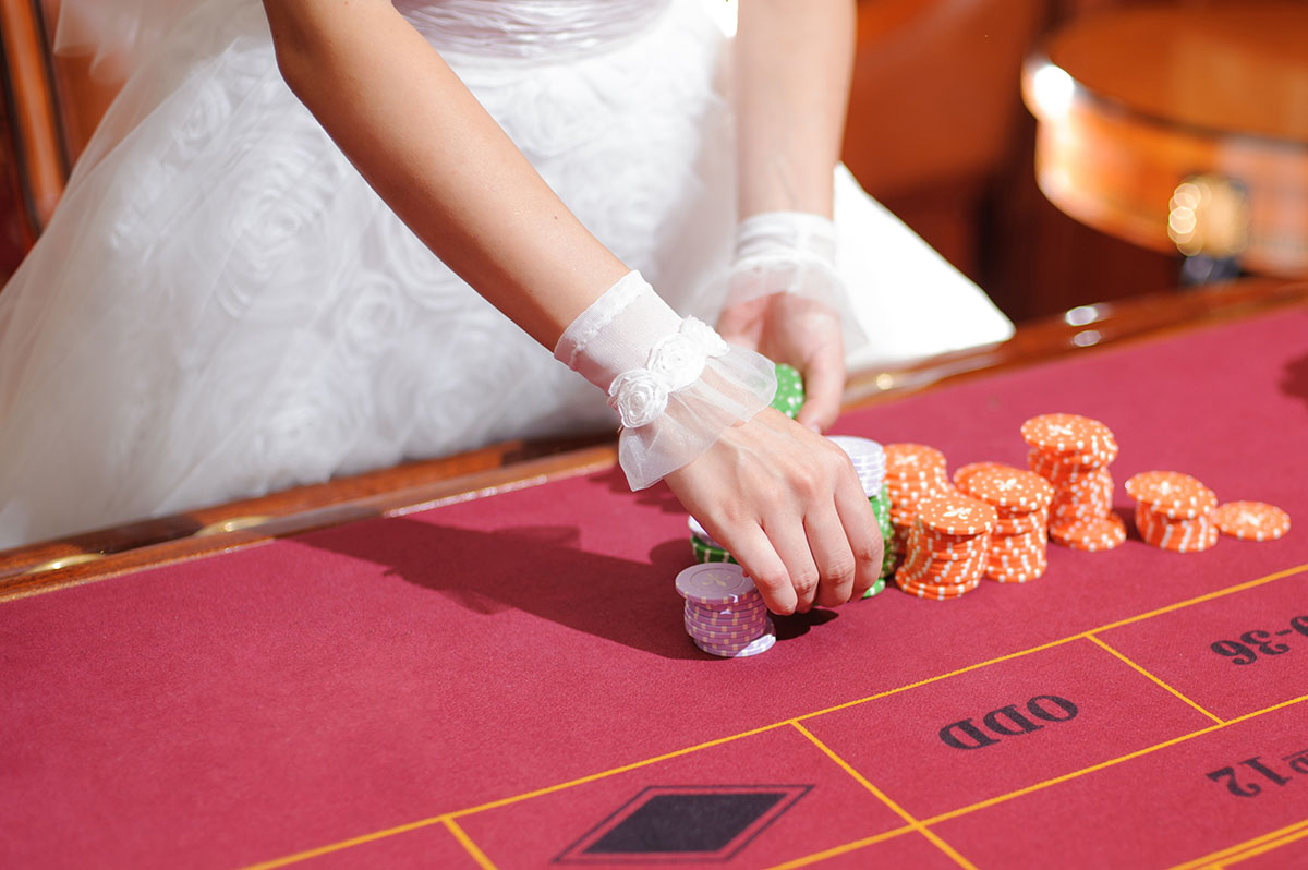Bride in wedding dress holding chips at fun casino roulette table