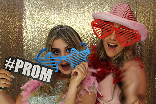 Two teenage girls in fancy dress, holding up a sign saying Prom