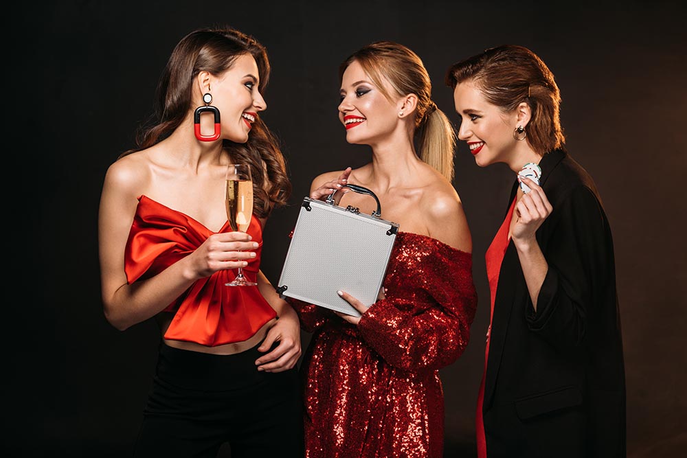 Three glamorous young ladies dressed for a night out and holding drinks and poker chips